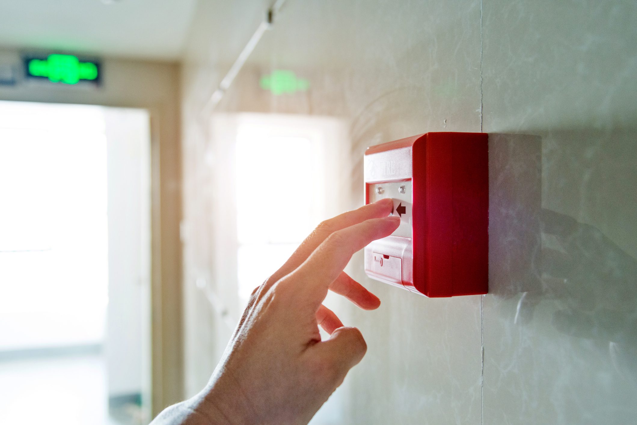 Hand pressing red fire alarm button.