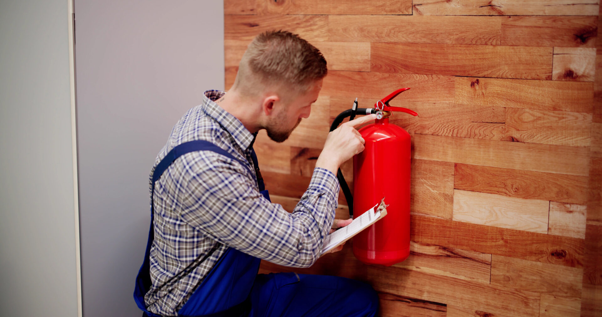 Man inspecting a wall-mounted fire extinguisher.