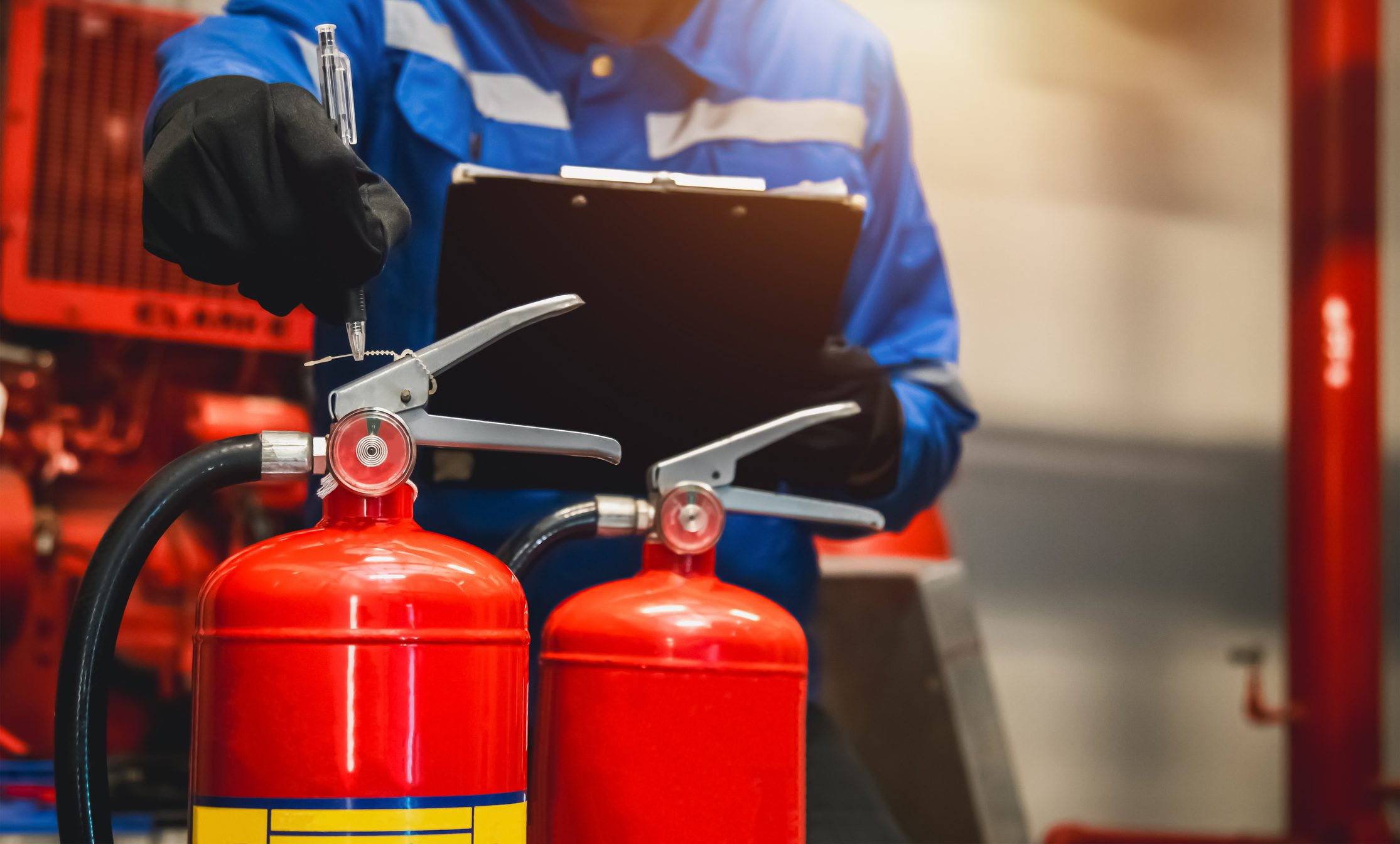 Person inspecting fire extinguishers with clipboard.