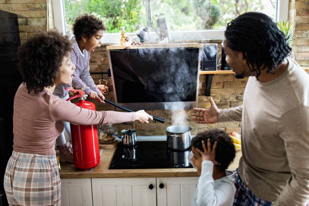 African American family using fire extinguisher while spraying smoke from a saucepan in the kitchen. Focus is on shocked girl.
