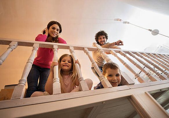 Low angle view of smiling family leaning on banister at home and looking at camera.
